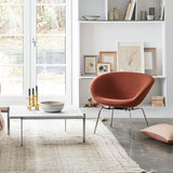A rust-orange bowl-shaped lounge chair on slim chrome legs beside a marble coffee table by a white bookcase