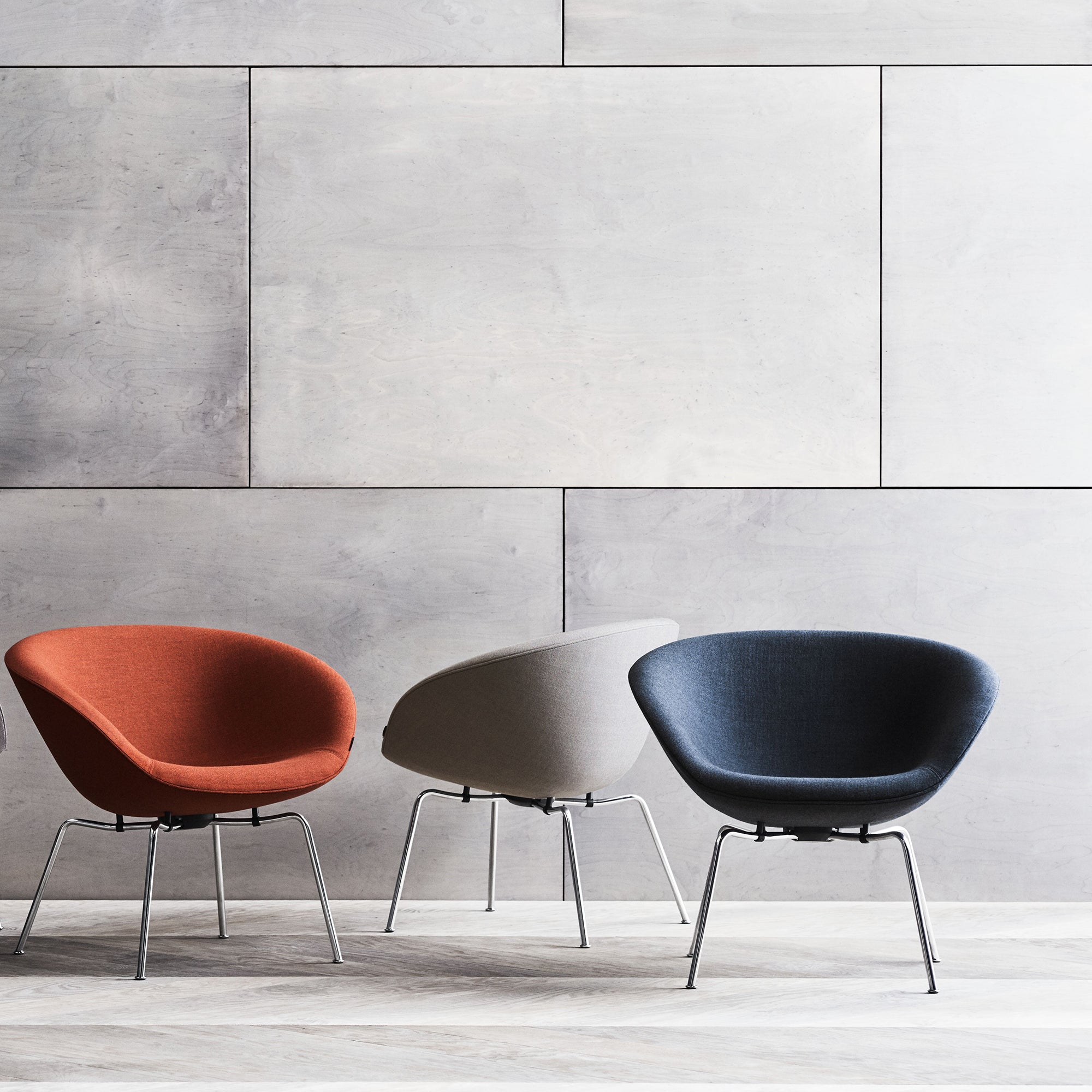 Three rounded bowl-shaped lounge chairs in rust orange, pale grey and navy on slim chrome legs