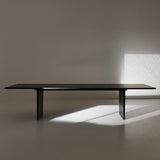 A long black wooden table on two slab legs in a bare room with sunlight on the floor