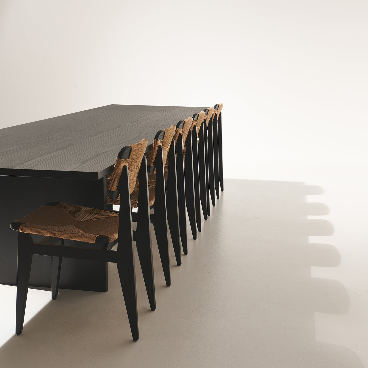 A long dark wood table with a row of black chairs with woven natural rush seats and backs