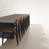 A long dark wood table with a row of black chairs with woven natural rush seats and backs