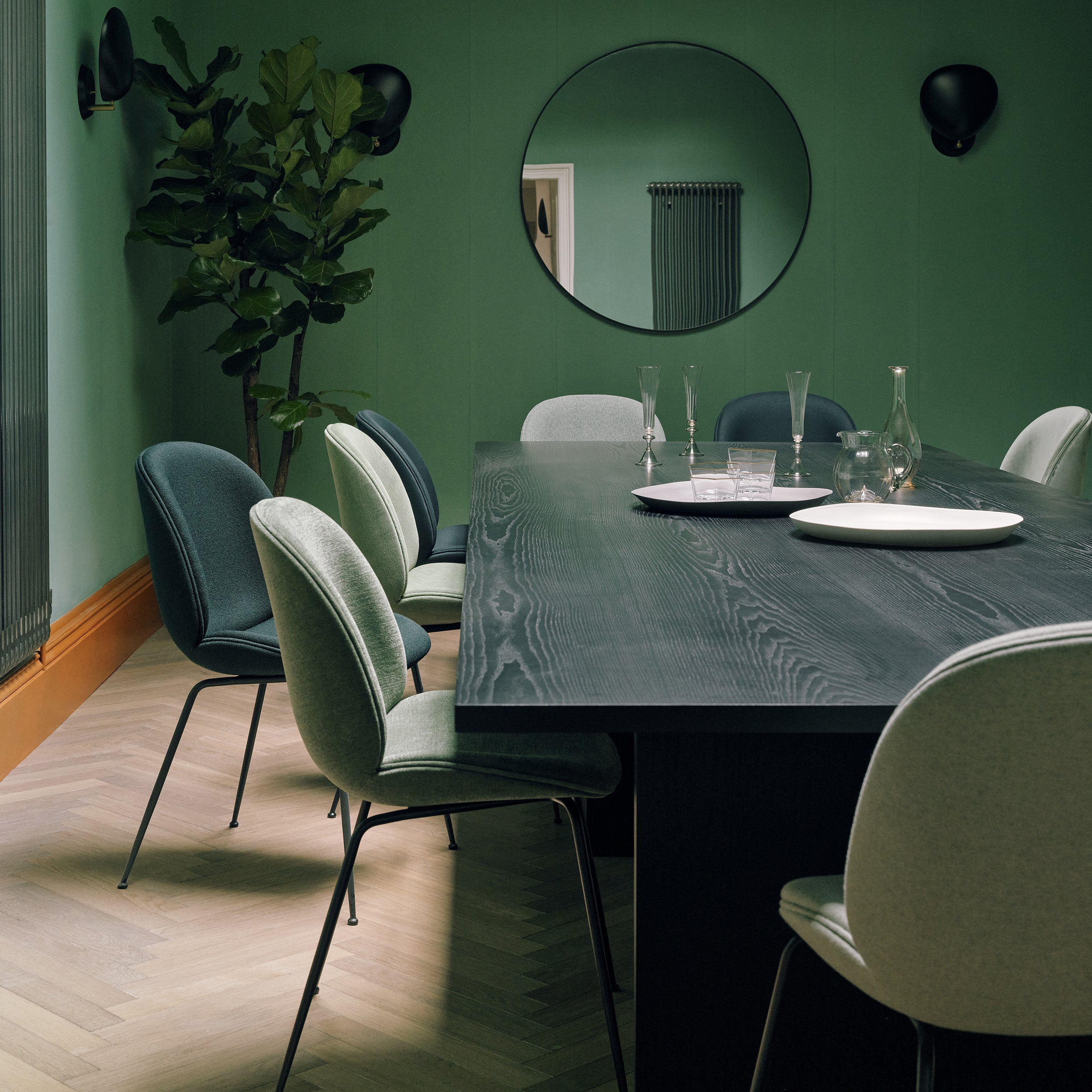A long dark wood dining table with green and grey upholstered chairs in a green room