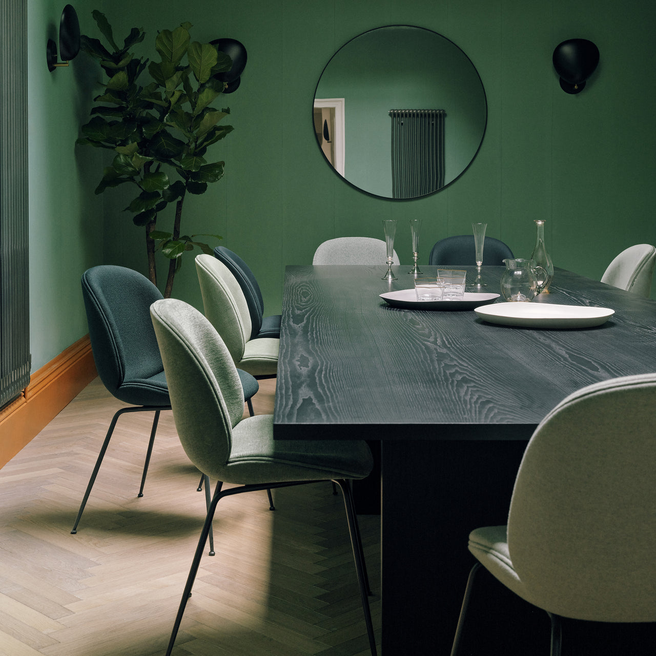 A long dark wood dining table with green and grey upholstered chairs in a green room
