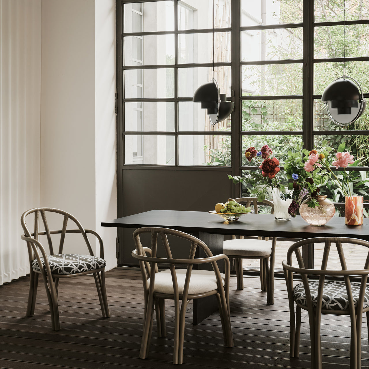 A long dark wood dining table with bentwood armchairs, patterned and cream seats, beside a glass-paned door