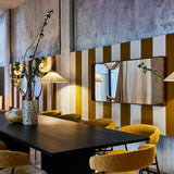 A long black dining table with mustard curved-back chairs, a speckled vase and a wide mirror on a striped wall