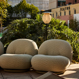 A slim outdoor floor lamp with a ribbed oval shade stands between two rounded green chevron armchairs