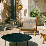 A tall black floor lamp with a yellow ribbed shade beside a rope-seat wooden chair on a sunlit terrace