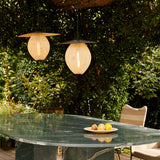 Two glowing woven pendant lamps with flat dark shades hang over a green marble table outdoors