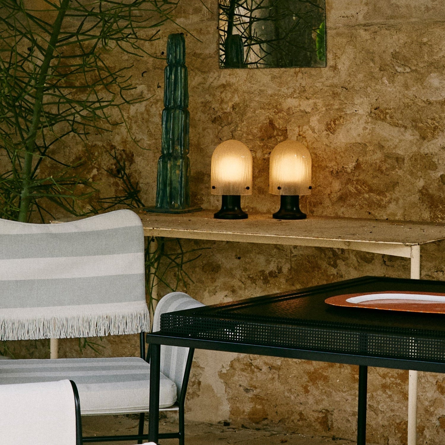 Two small glowing domed lamps with black bases on a narrow table against a rough stone wall