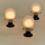 Three glowing table lamps with ribbed frosted glass domes on dark round pedestal bases