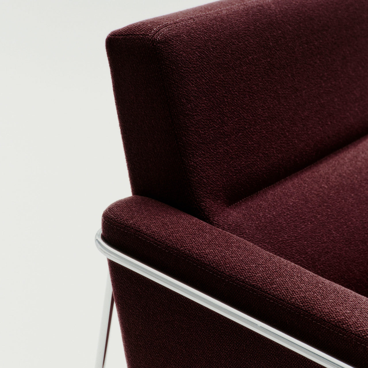 Close-up of a deep burgundy woven fabric armchair corner with a slim polished chrome frame