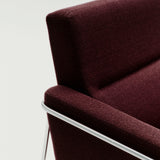 Close-up of a deep burgundy woven fabric armchair corner with a slim polished chrome frame