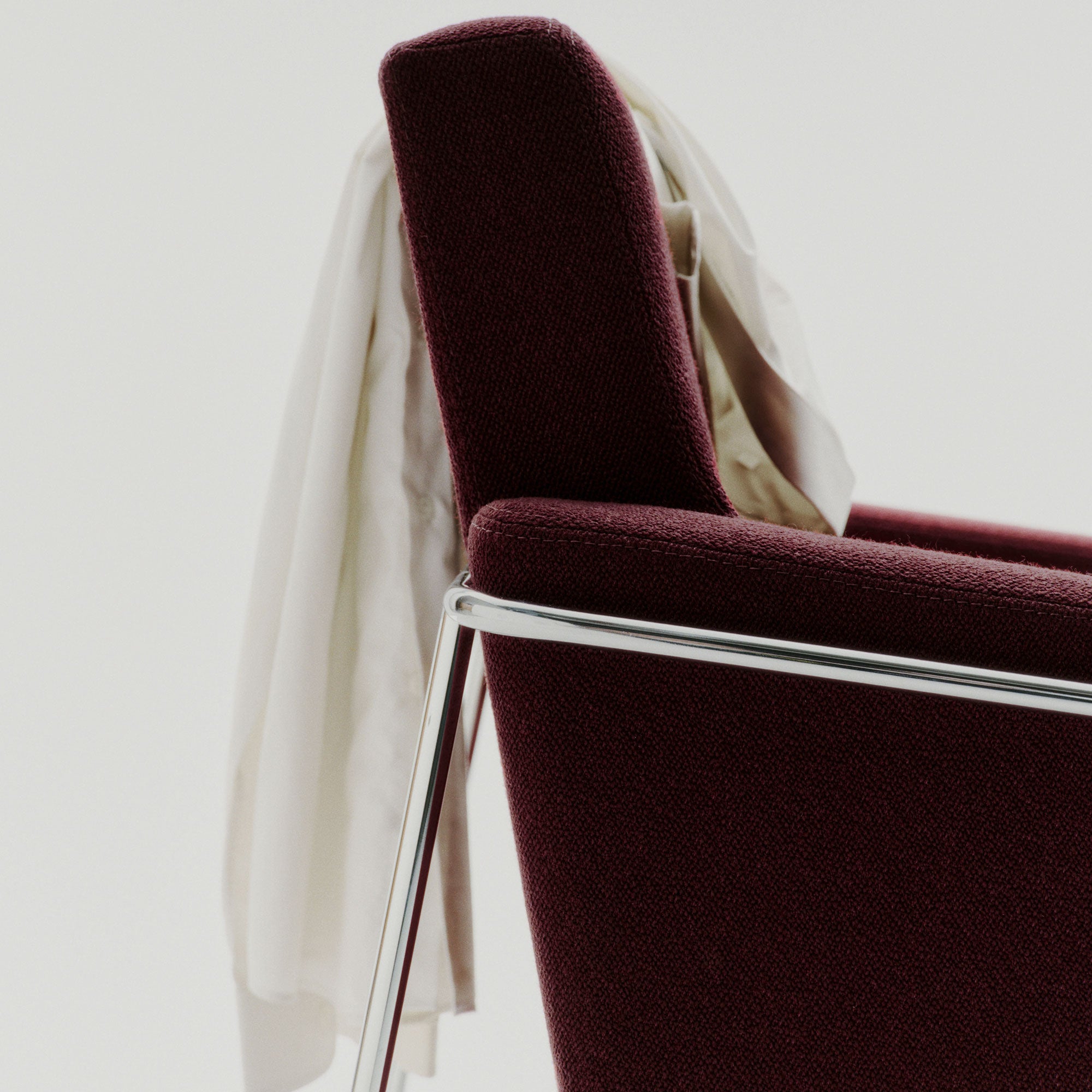 Close-up of a burgundy fabric armchair with a chrome tube frame and a cream shirt draped over the back