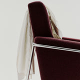 Close-up of a burgundy fabric armchair with a chrome tube frame and a cream shirt draped over the back