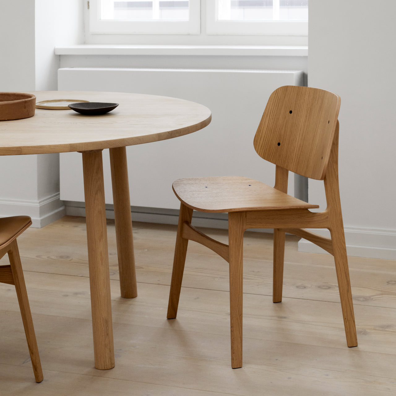 A light oak dining chair with a curved wooden back and seat beside a round oak table