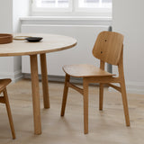 A light oak dining chair with a curved wooden back and seat beside a round oak table