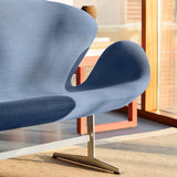 Close-up of a curved blue fabric sofa on a satin metal pedestal base, beside a red-orange side table