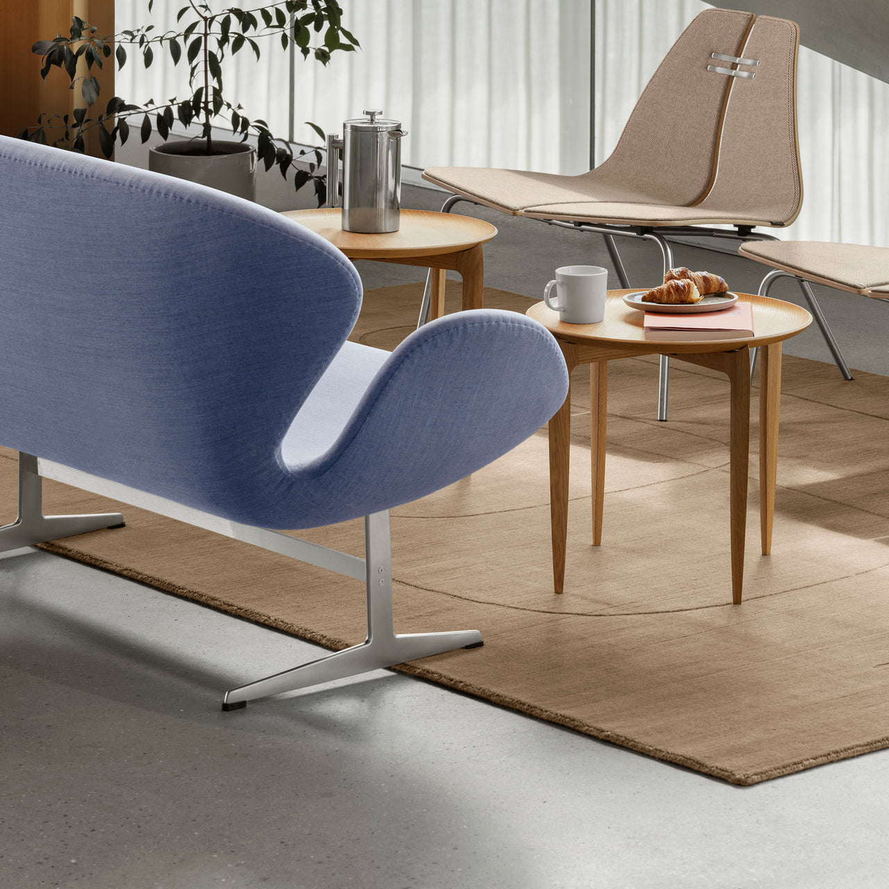 A curved sofa in pale blue fabric on a metal base, beside a round wooden side table and a tan rug