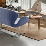 A curved sofa in pale blue fabric on a metal base, beside a round wooden side table and a tan rug