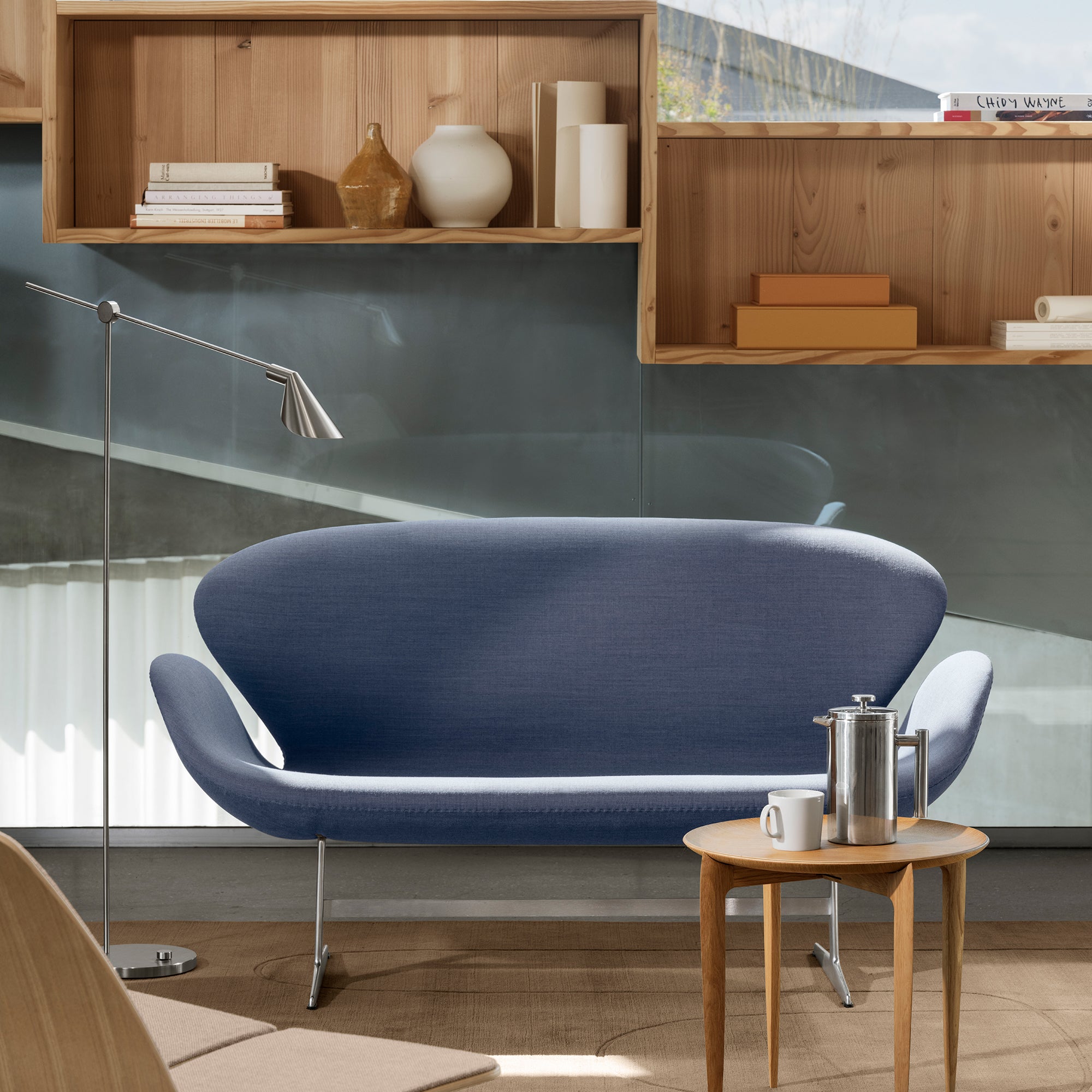 A curved blue-grey fabric sofa on slim metal legs beside a small round wooden side table