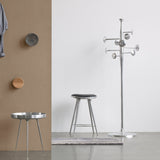 A polished aluminium coat stand with round pegs beside a metal stool and a three-legged side table