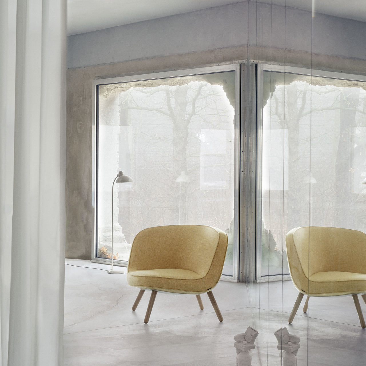 A rounded yellow fabric lounge chair on light wooden legs in a concrete room with large windows