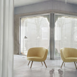 A rounded yellow fabric lounge chair on light wooden legs in a concrete room with large windows