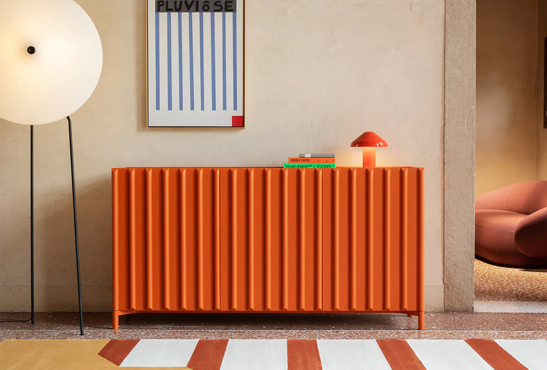 Orange sideboard in a room with a lamp and abstract art on the wall.