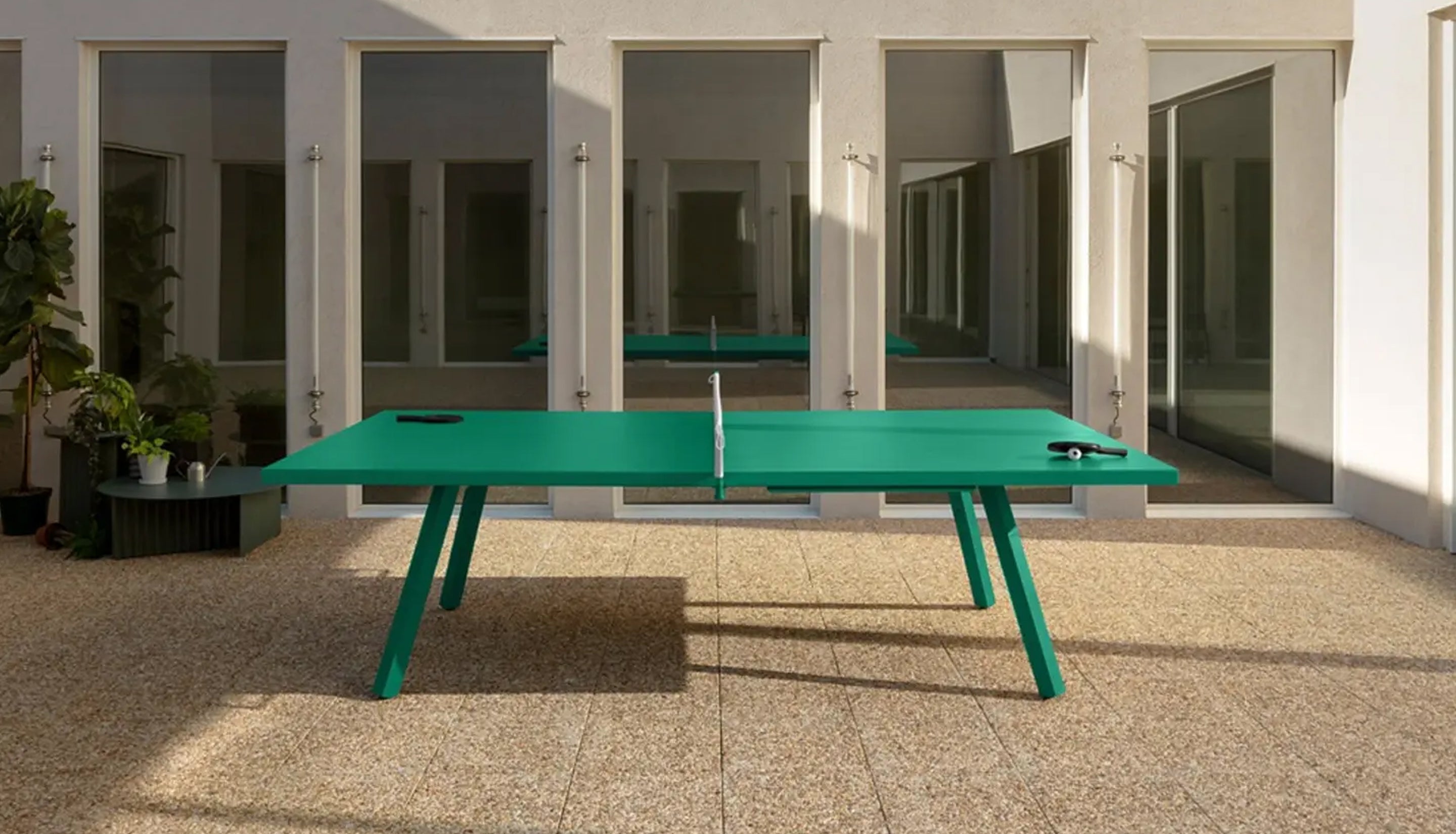 Green ping pong table in an outdoor setting with a modern building in the background