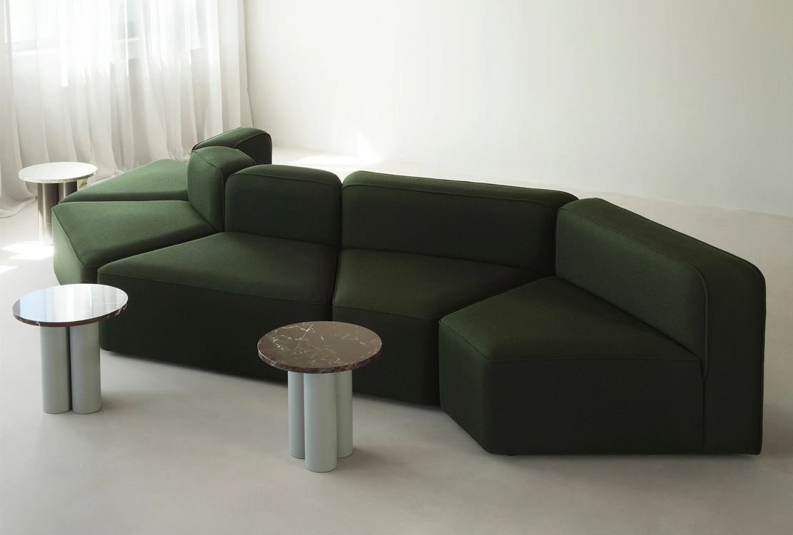 A dark green modular upholstered sectional sofa in a minimalist room, styled with three small accent tables.