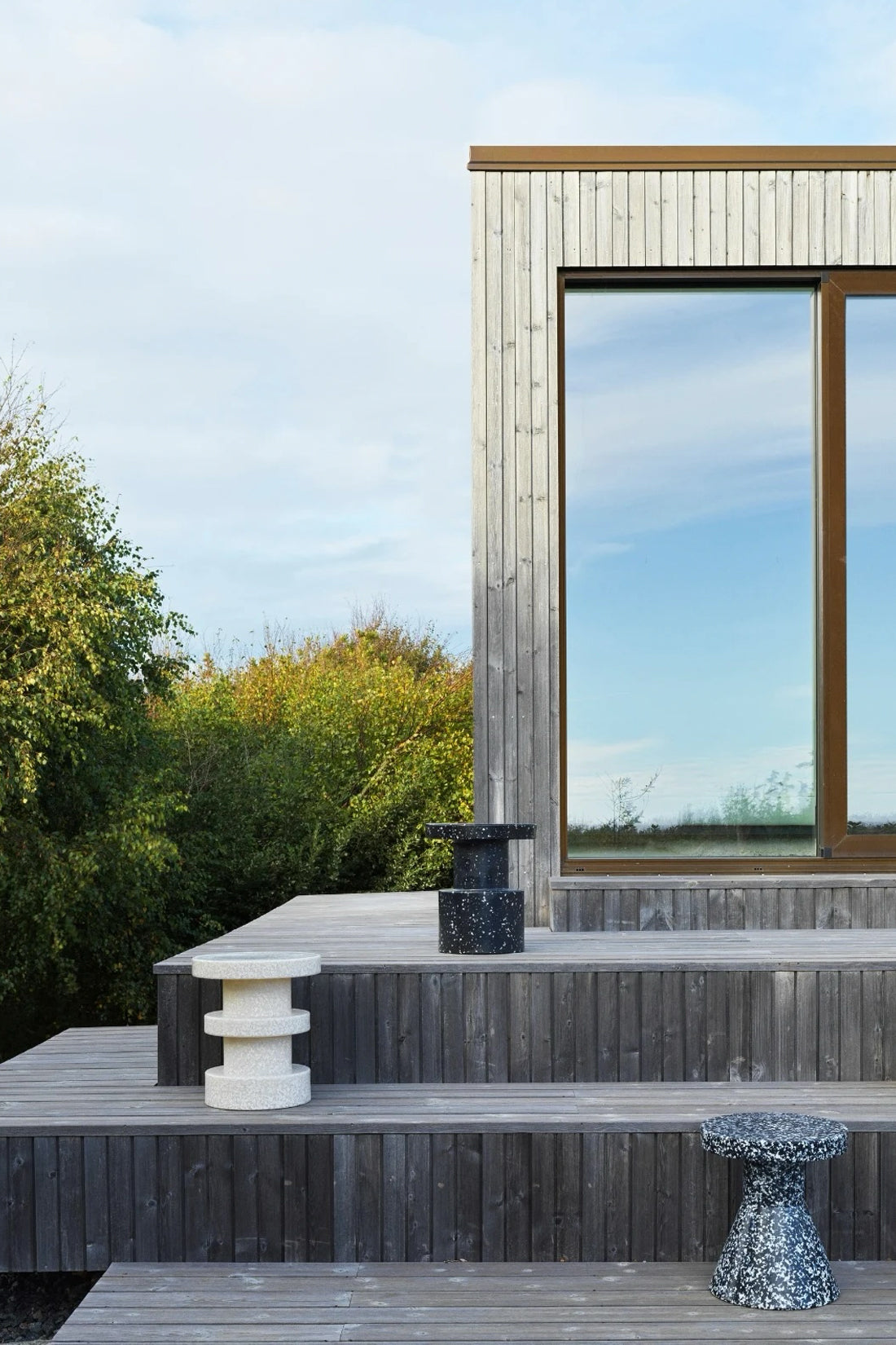 Three modern recycled stools in different textures and colors (white speckled, black speckled, and dark gray) arranged on a wooden deck outdoors.