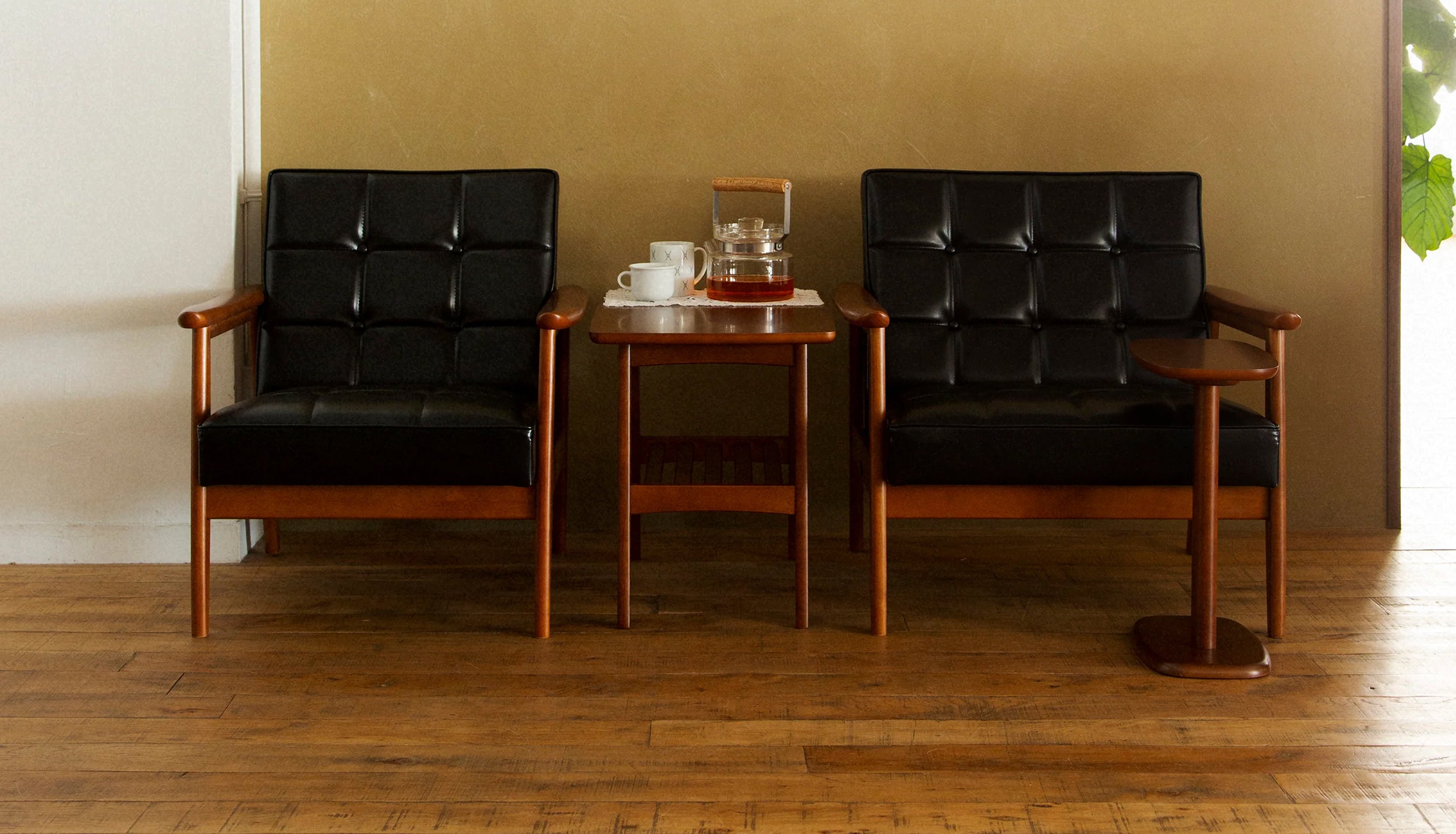 Two black leather chairs with wood frames and a wooden side table between them sit with teapot and cups.