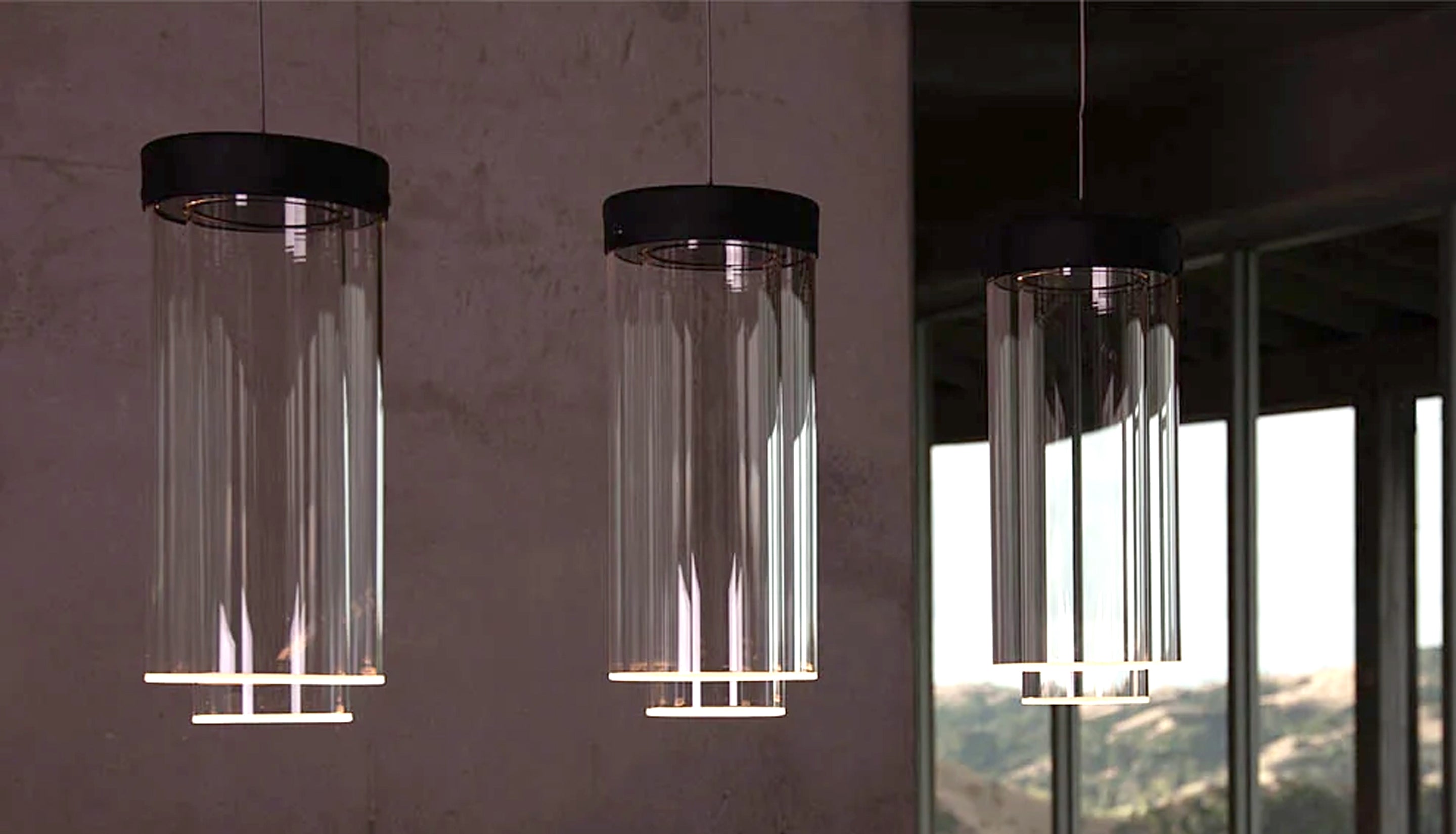 Three modern cylindrical pendant lights with clear glass shades and black metal caps hanging in a minimalist interior setting.