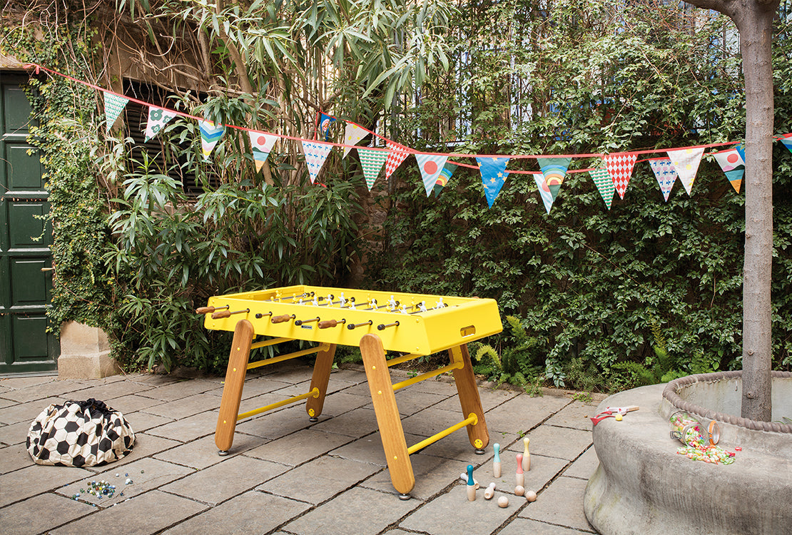 Yellow foosball table in a garden with bunting and children's toys.