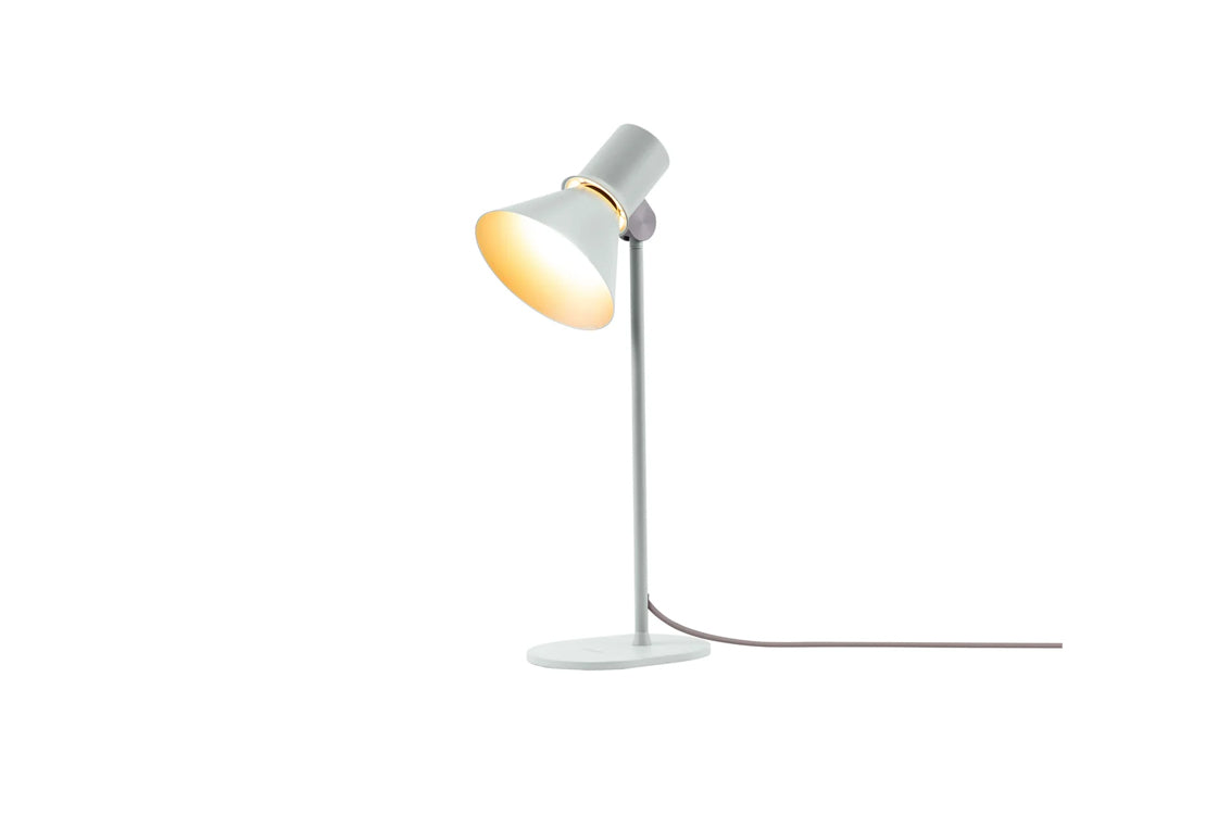 A modern adjustable desk lamp with a white metal shade and stand, featuring a warm yellow glow from the illuminated bulb inside the cone-shaped shade, on a solid white background.