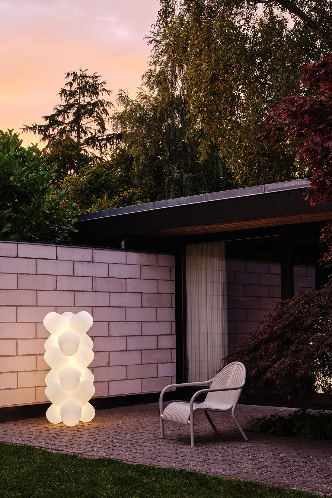 Modern outdoor setting with a light sculpture and chair near a building.
