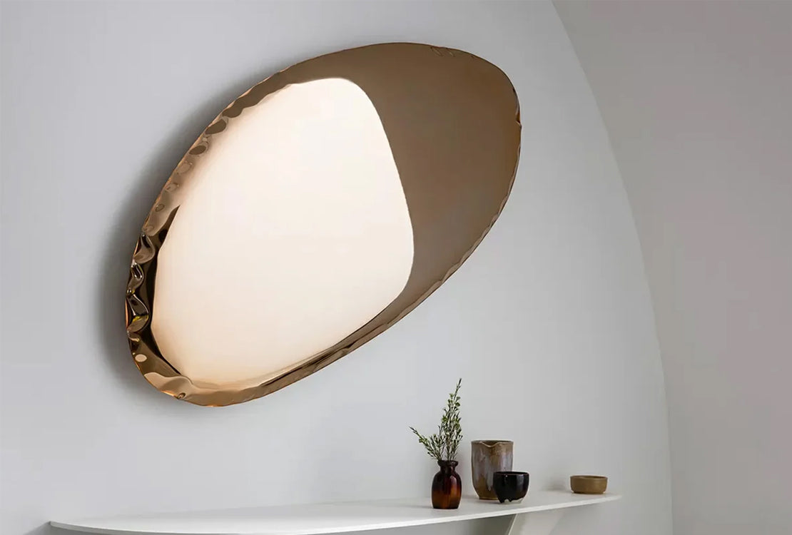 Reflective wall decor on a plain wall with decorative items below.