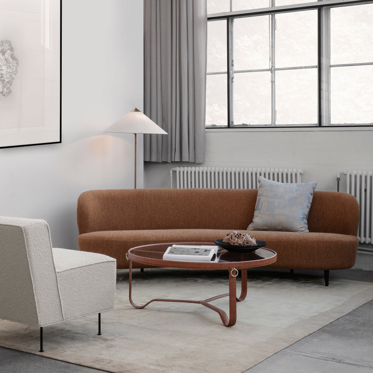 A round glass-topped coffee table with a tan leather frame in front of a curved rust-brown sofa
