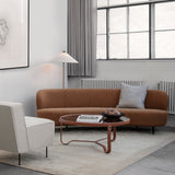 A round glass-topped coffee table with a tan leather frame in front of a curved rust-brown sofa