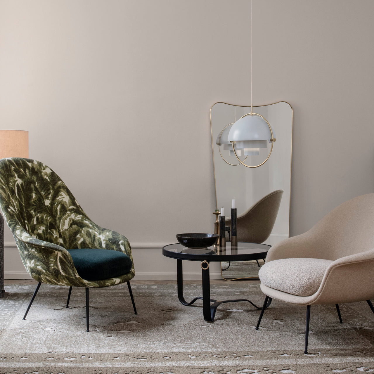 A round glass-topped coffee table with a black leather-wrapped base between two lounge chairs in a pale room