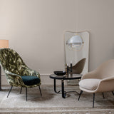 A round glass-topped coffee table with a black leather-wrapped base between two lounge chairs in a pale room