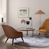 A round glass coffee table with a leather-wrapped frame between two armchairs on a grey rug