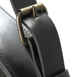 Close-up of a thick black leather strap threaded through an aged brass buckle on a mirror frame