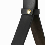 Close-up of two black leather straps crossing, held together by a small brass snap fastener