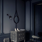 A round mirror with a black leather strap hangs on a navy wall above a patterned chest of drawers