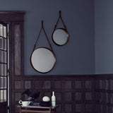 Two round mirrors with brown leather straps hang on a blue-grey wall above dark wood panelling