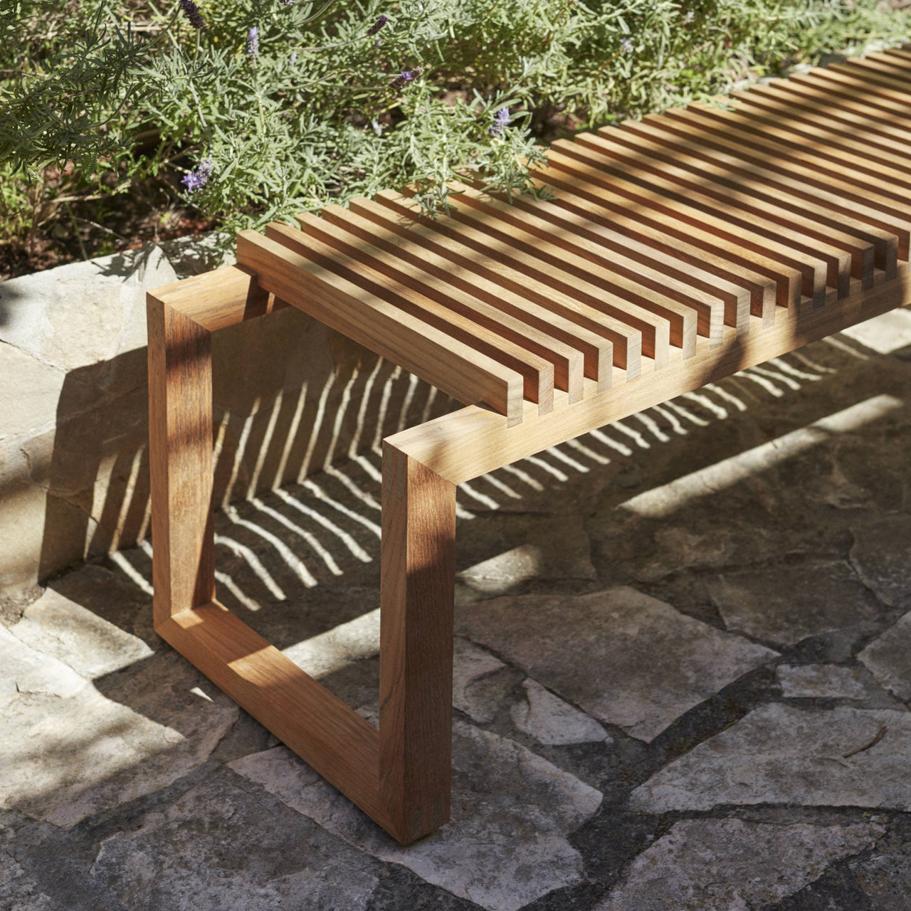 Outdoor Cutter Bench by Skagerak with wooden slats and rectangular frame on stone patio.