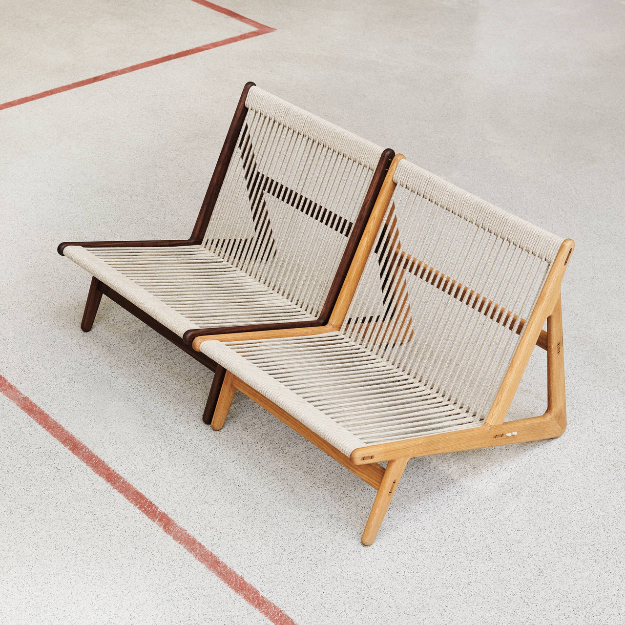 Two low lounge chairs with cream rope-woven seats and backs, one dark wood, one light oak, on a speckled floor