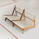 Two low lounge chairs with cream rope-woven seats and backs, one dark wood, one light oak, on a speckled floor