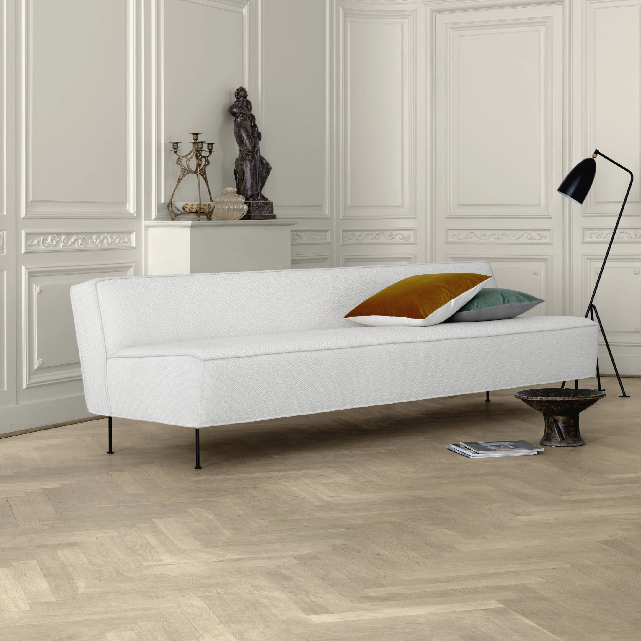 A low white fabric sofa on thin black legs in a panelled room with a herringbone wood floor